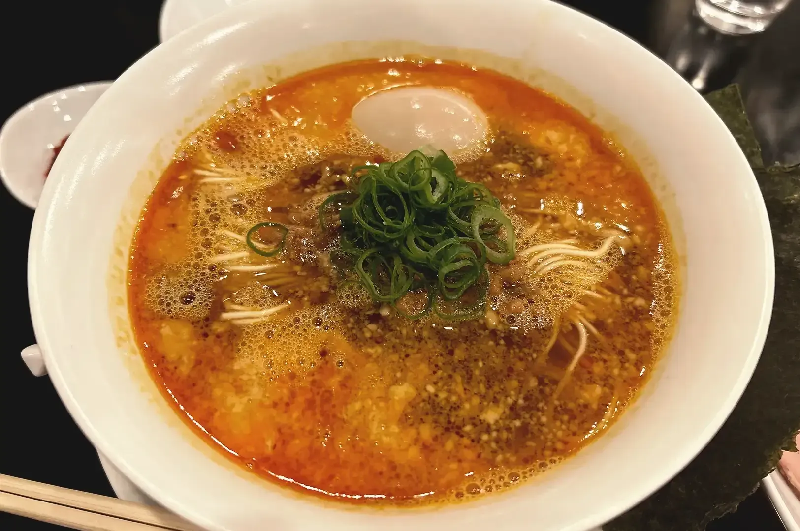 Ramen noodles drenched in flavorful broth with egg garnished with spring onions served on white bowl