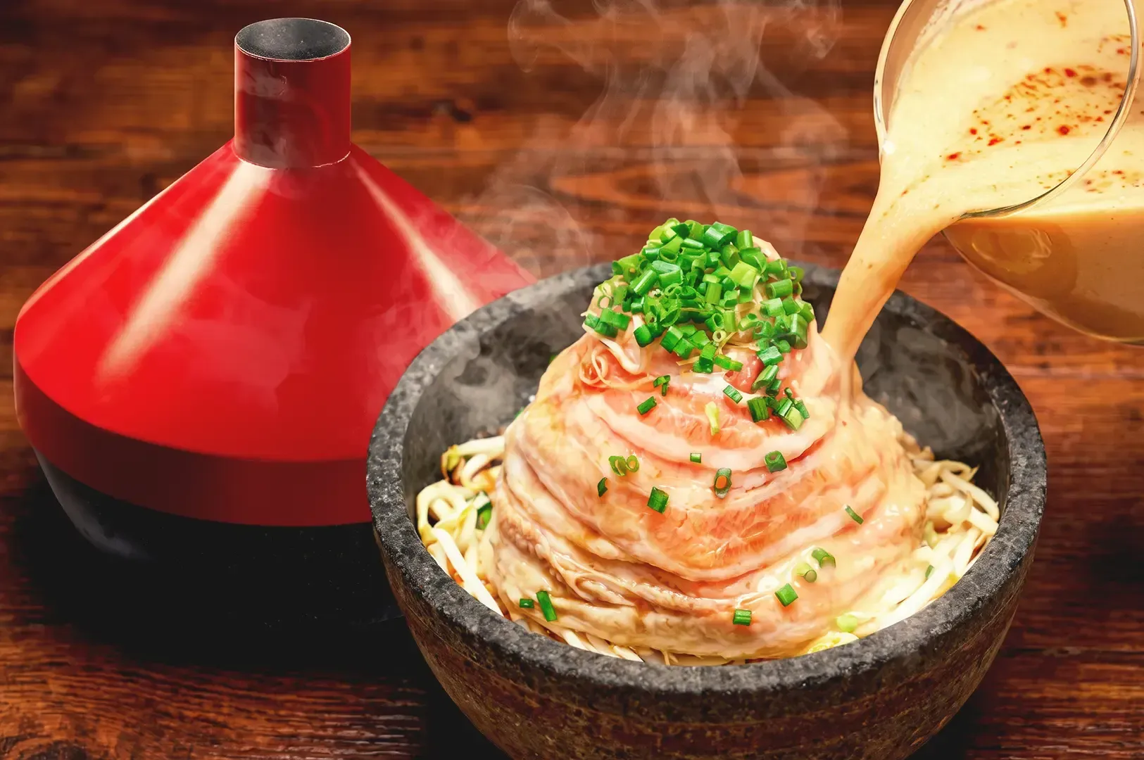 Creamy ramen broth being poured to a bowl of noodles topped with meat and garnished with spring onions