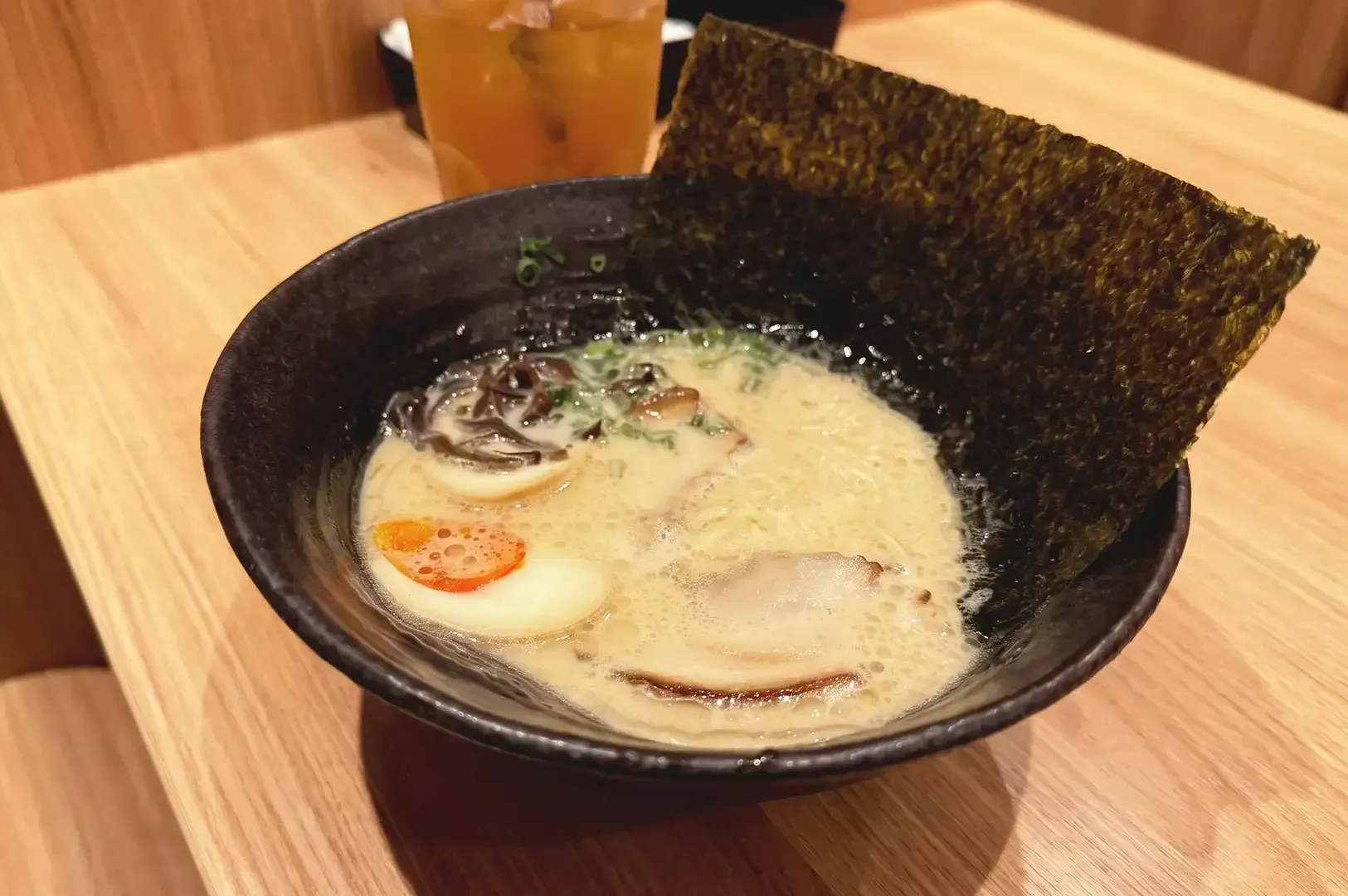 Creamy ramen both topped with spring onions, seaweed, boiled egg and pork meat in a black bowl