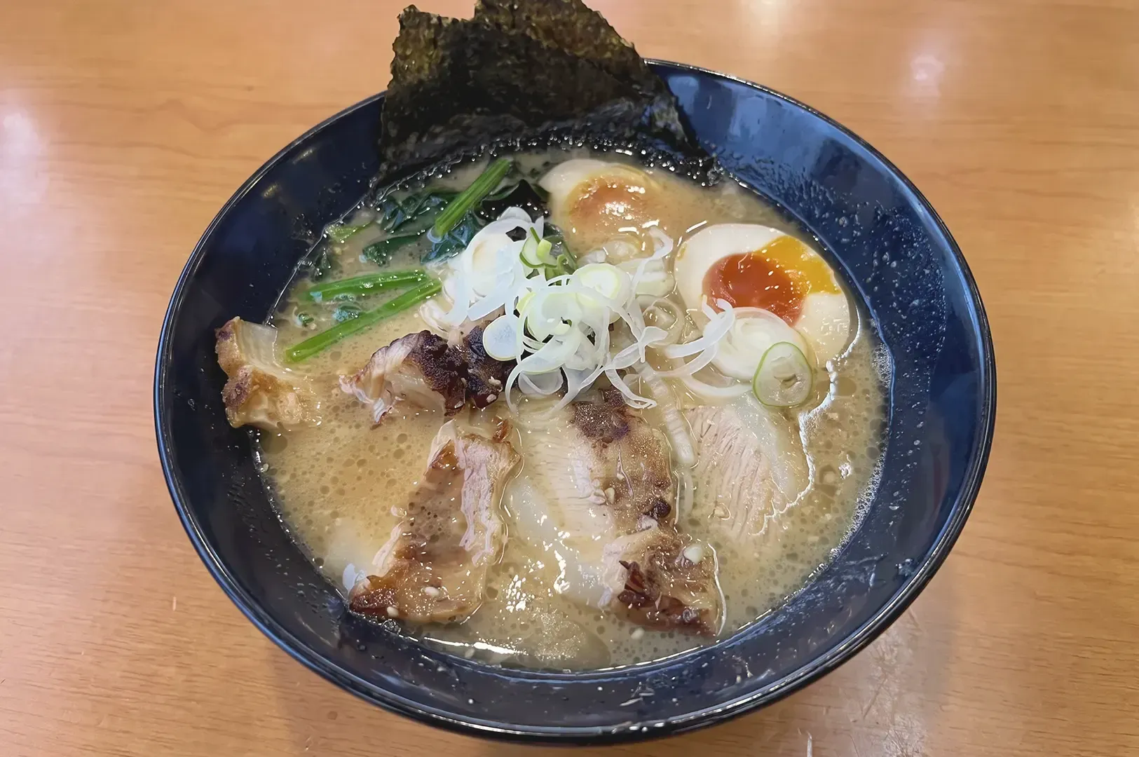 A bowl of ramen topped with egg, pork meat, onions, seaweed and other veggies