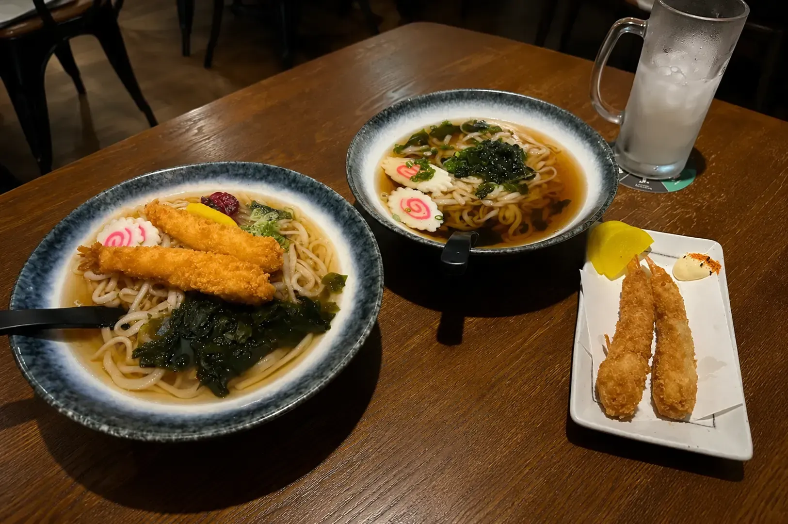 Two udon bowls with tempura shrimp and sides