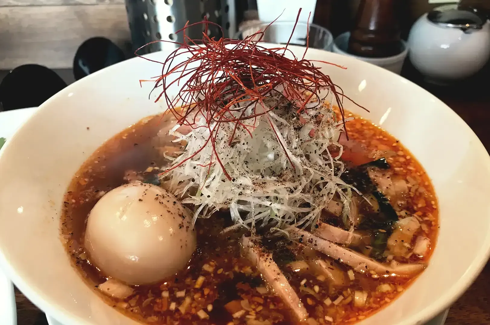 Ramen broth with egg, sliced pork meat garnished with shredded white and red vegetable served in white bowl