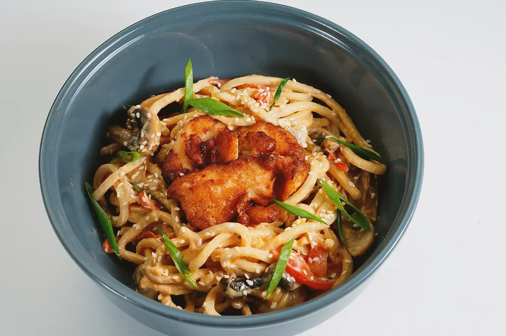 Bowl of fried udon noodles with fried chicken on the center seasoned with sesame seeds and green chives