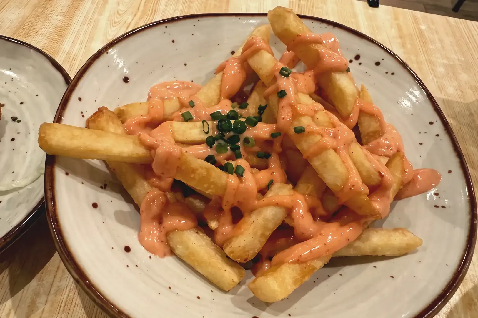 Potato fries drizzled with orange mayo sauce garnished with chopped green onions on a white ceramic plate