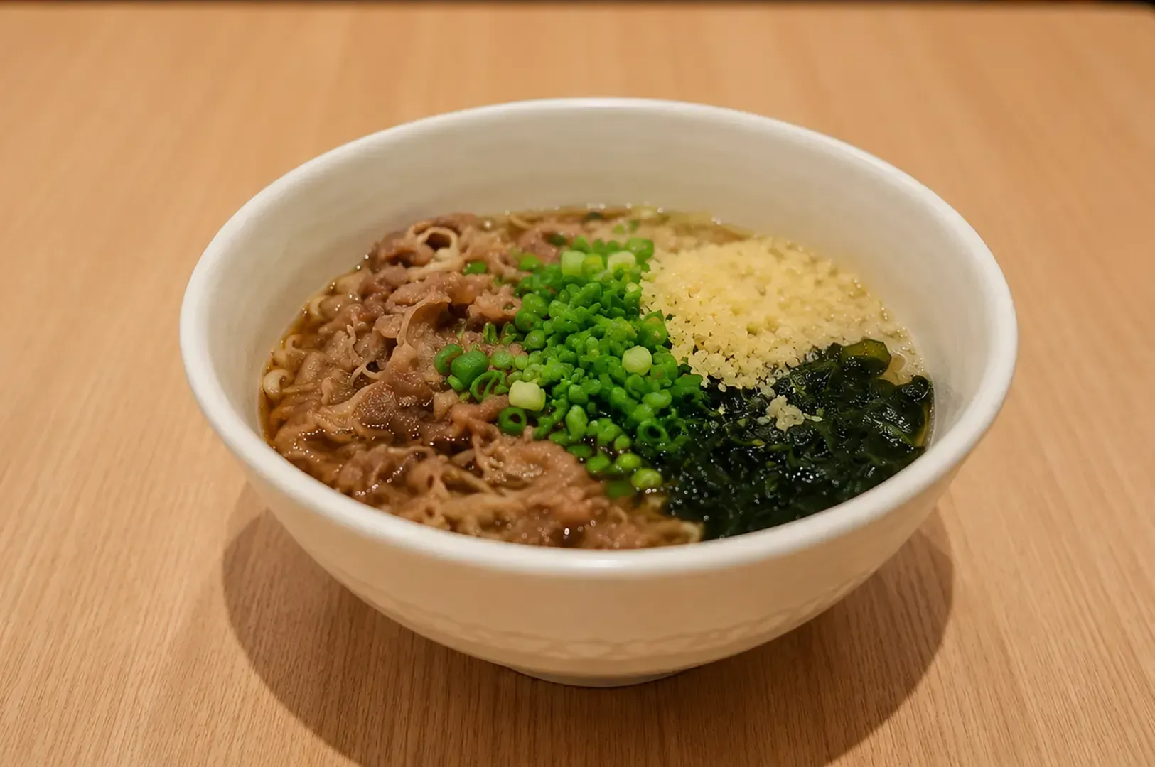 Bowl of beef udon noodle soup with a soft-boiled egg, seaweed, and green onions served on a wooden table