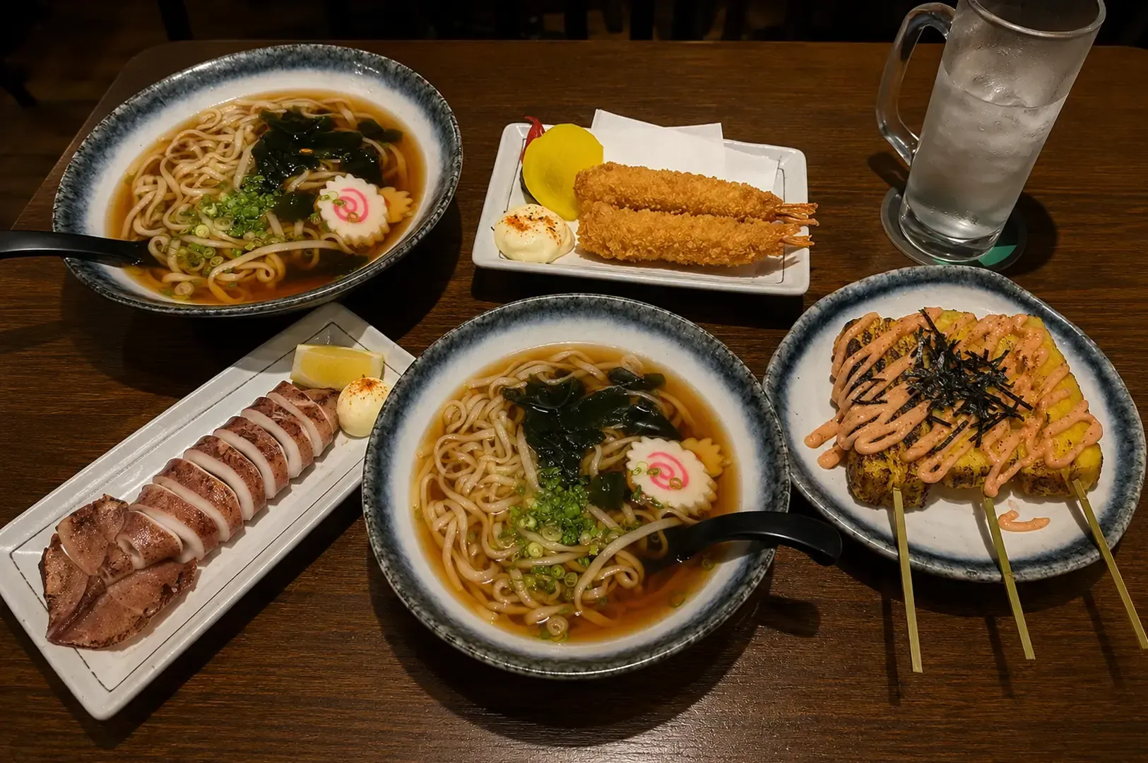 Japanese food spread with udon, sliced meat, and skewers