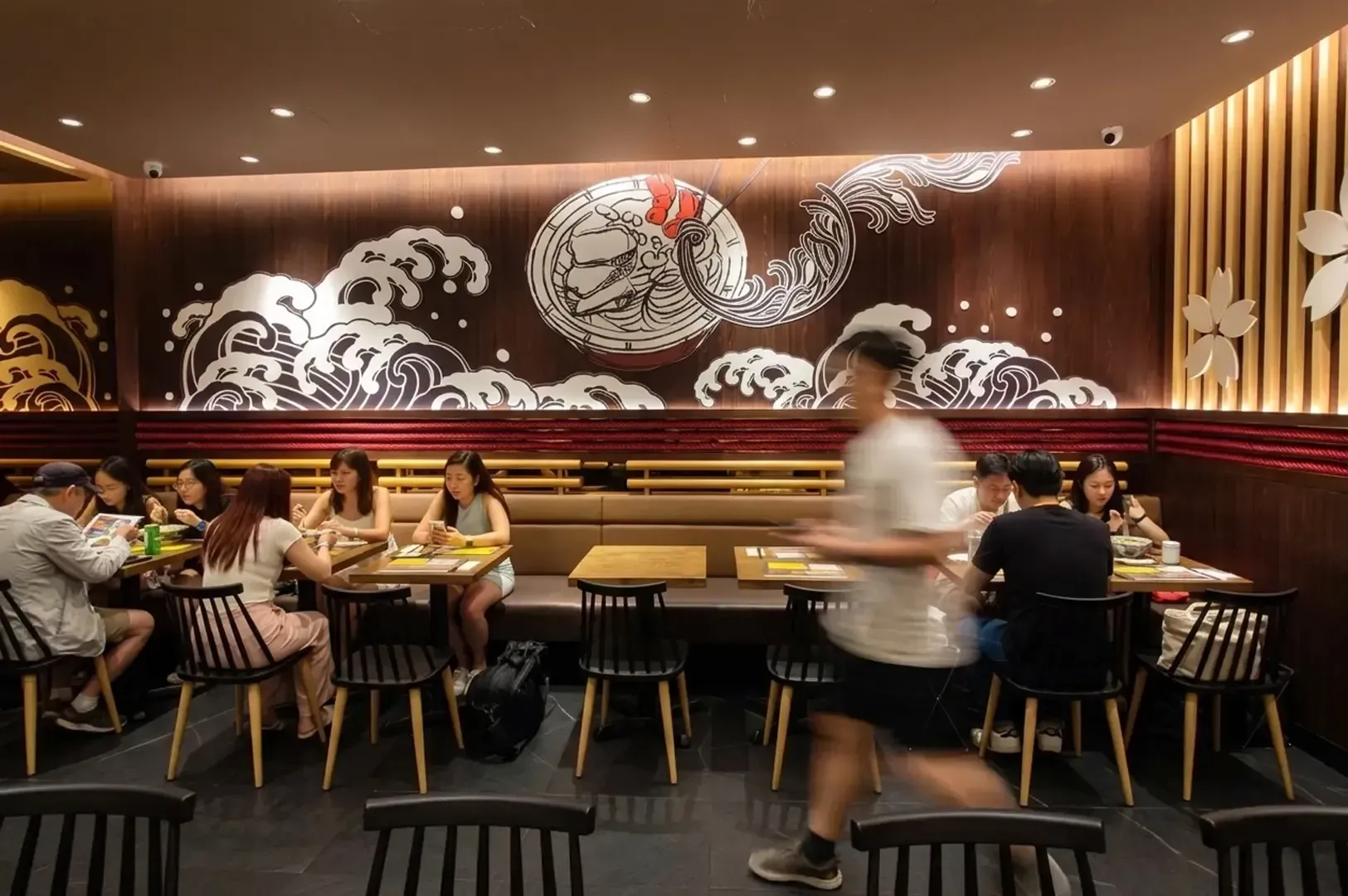 Dining area of Le Shrimp Ramen featuring a large wave and ramen bowl mural on the wall with customers eating