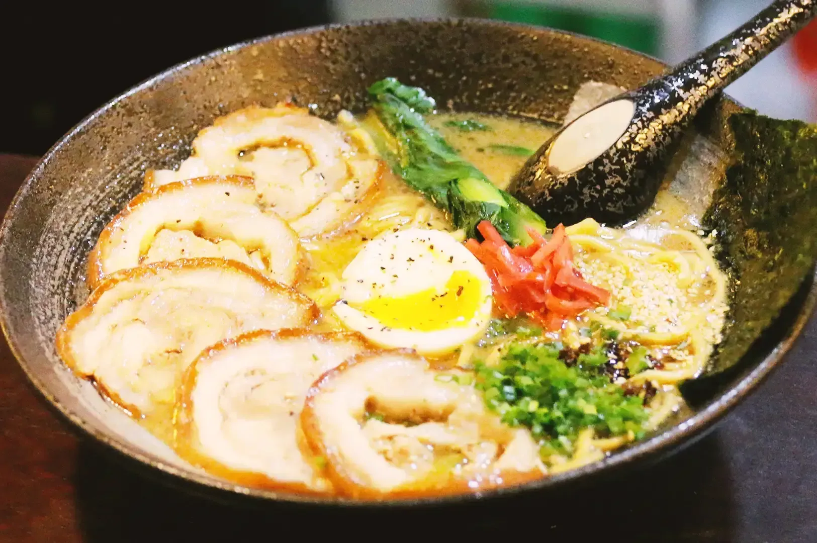 Close up of ramen bowl with slices of pork meat, egg, cabbage. noodles and seaweed garnished with spring onions