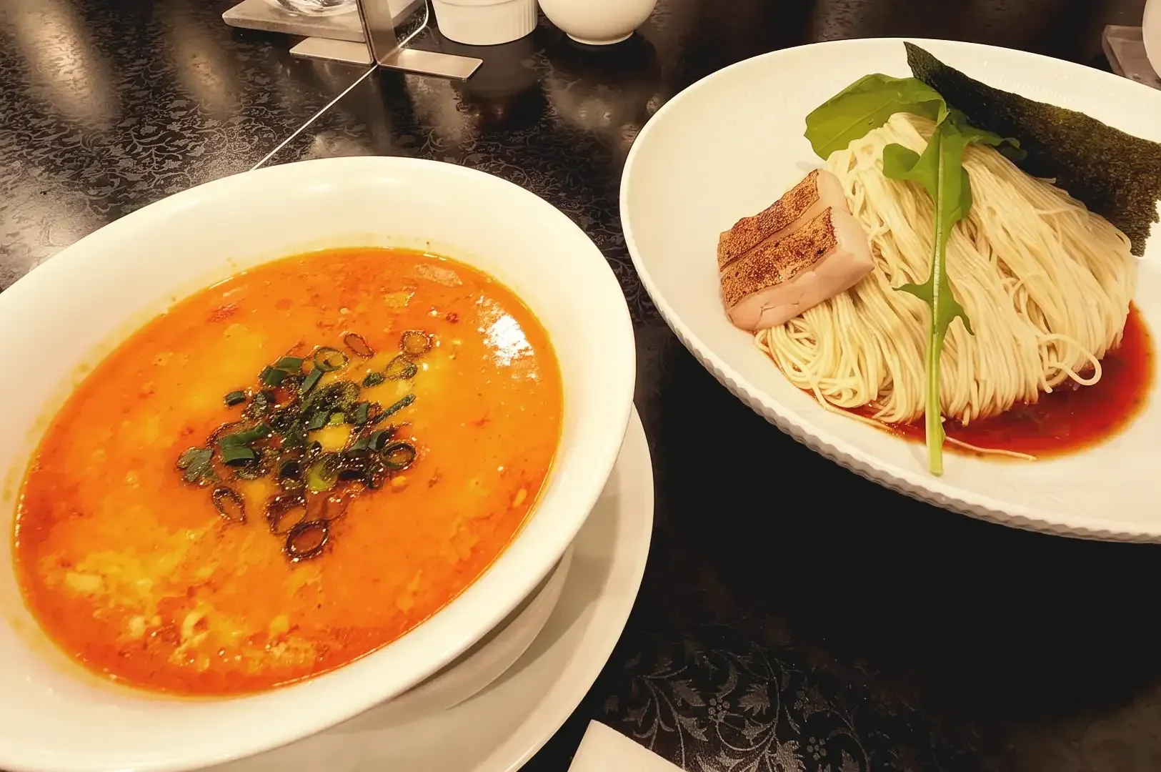 Separated ramen ingredients in two white bowls with pork meat slices garnished with green vegetable and spring onions
