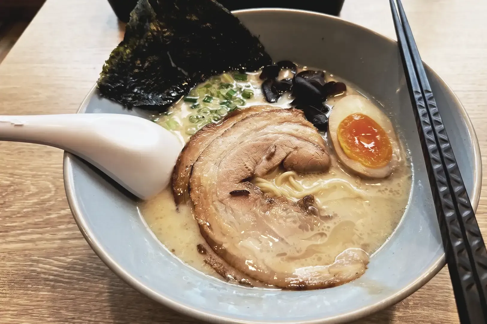 Bowl of creamy ramen with pork meat, seaweed, egg and black fungus garnishes with spring onions