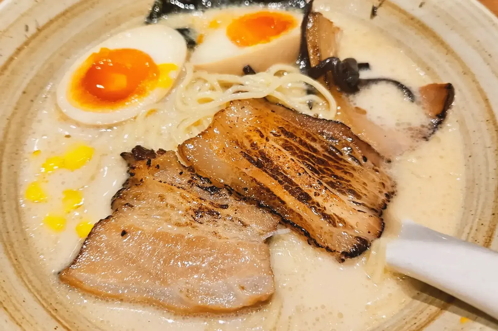 Ramen bowl containing slices of roasted pork, corn, eggs in half and seaweed drenched in creamy broth