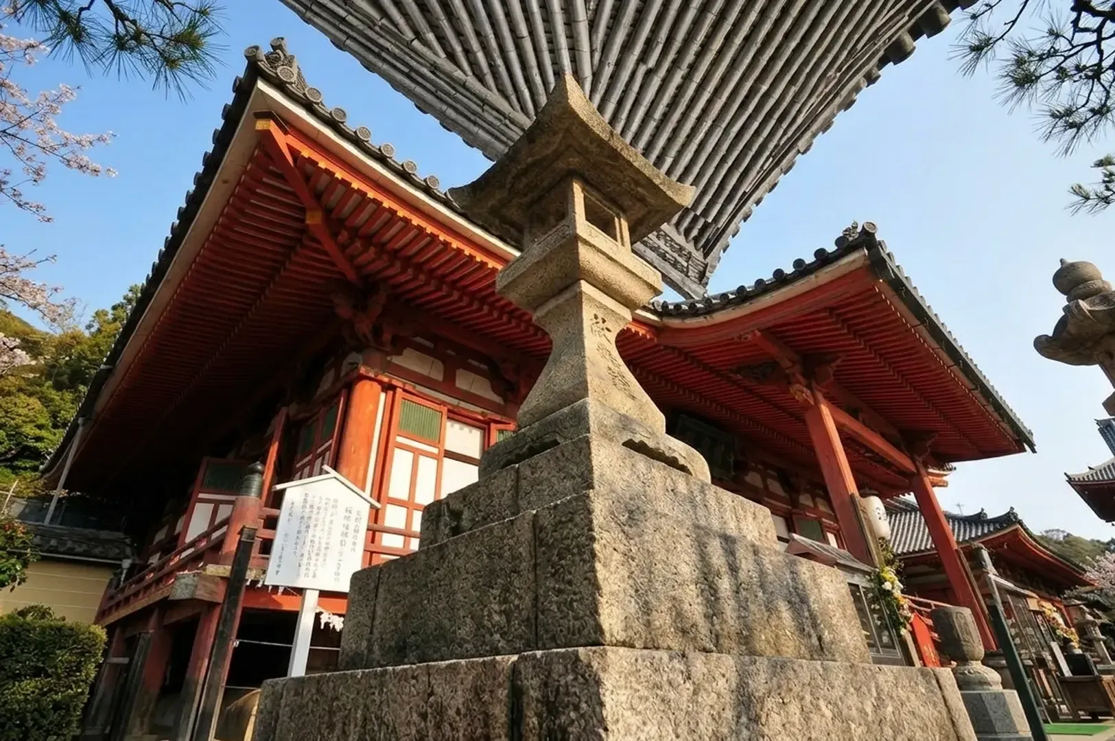 Traditional Japanese temple architecture in Onomichi with red-lacquered buildings, stone lantern, and cherry blossoms representing the historic port city