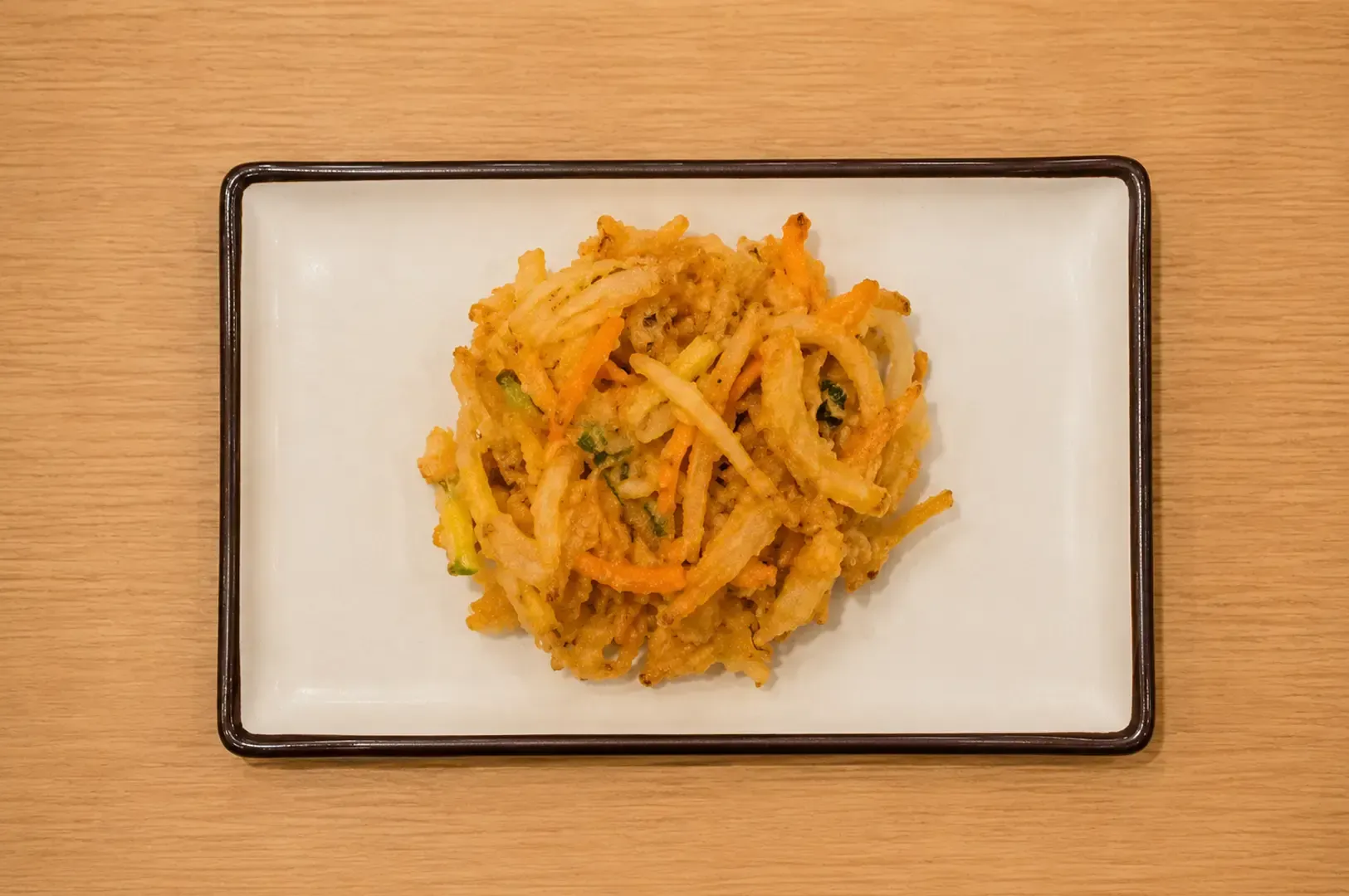 Crispy mixed vegetable tempura fritter piled on a rectangular white plate on a wooden table