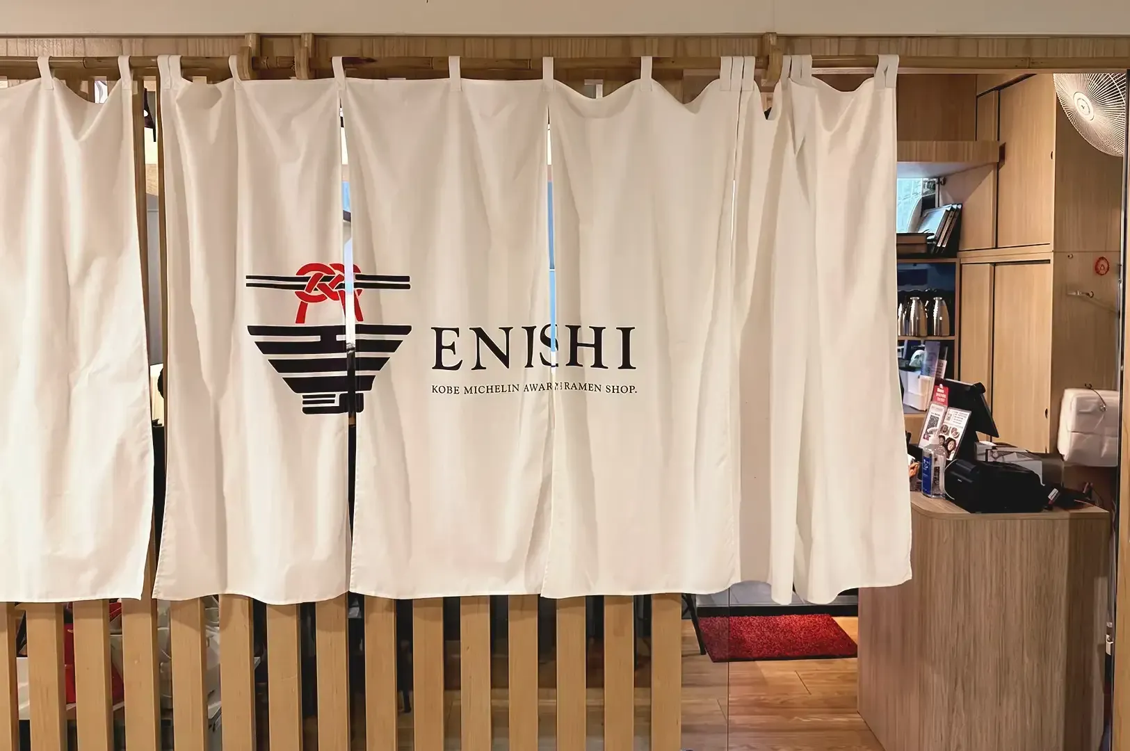 White curtain cloth with printed logo of Enishi covering the wooden motif interior of the store