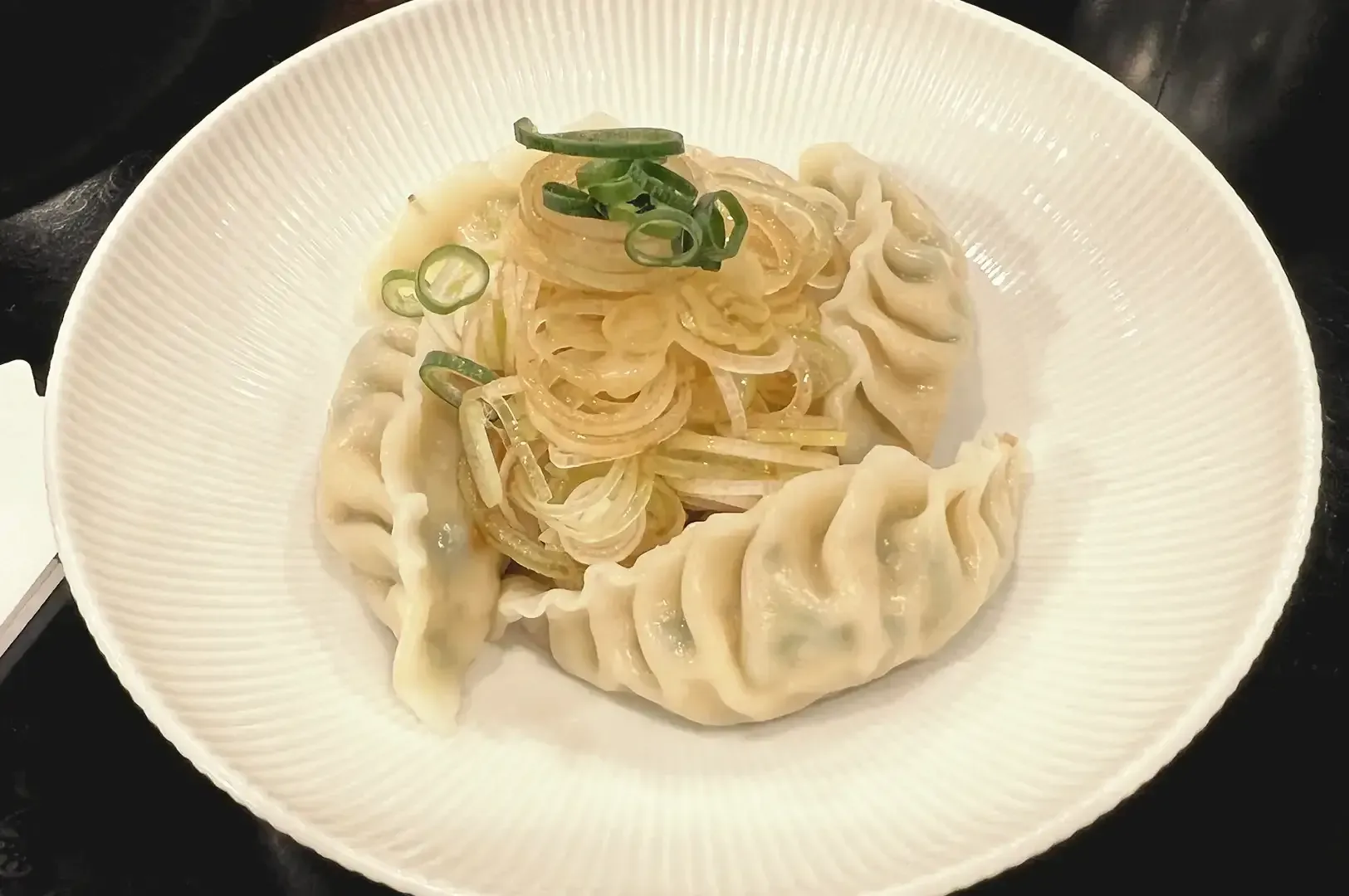 Shrimp wontons garnished with spring onions served in a white plate