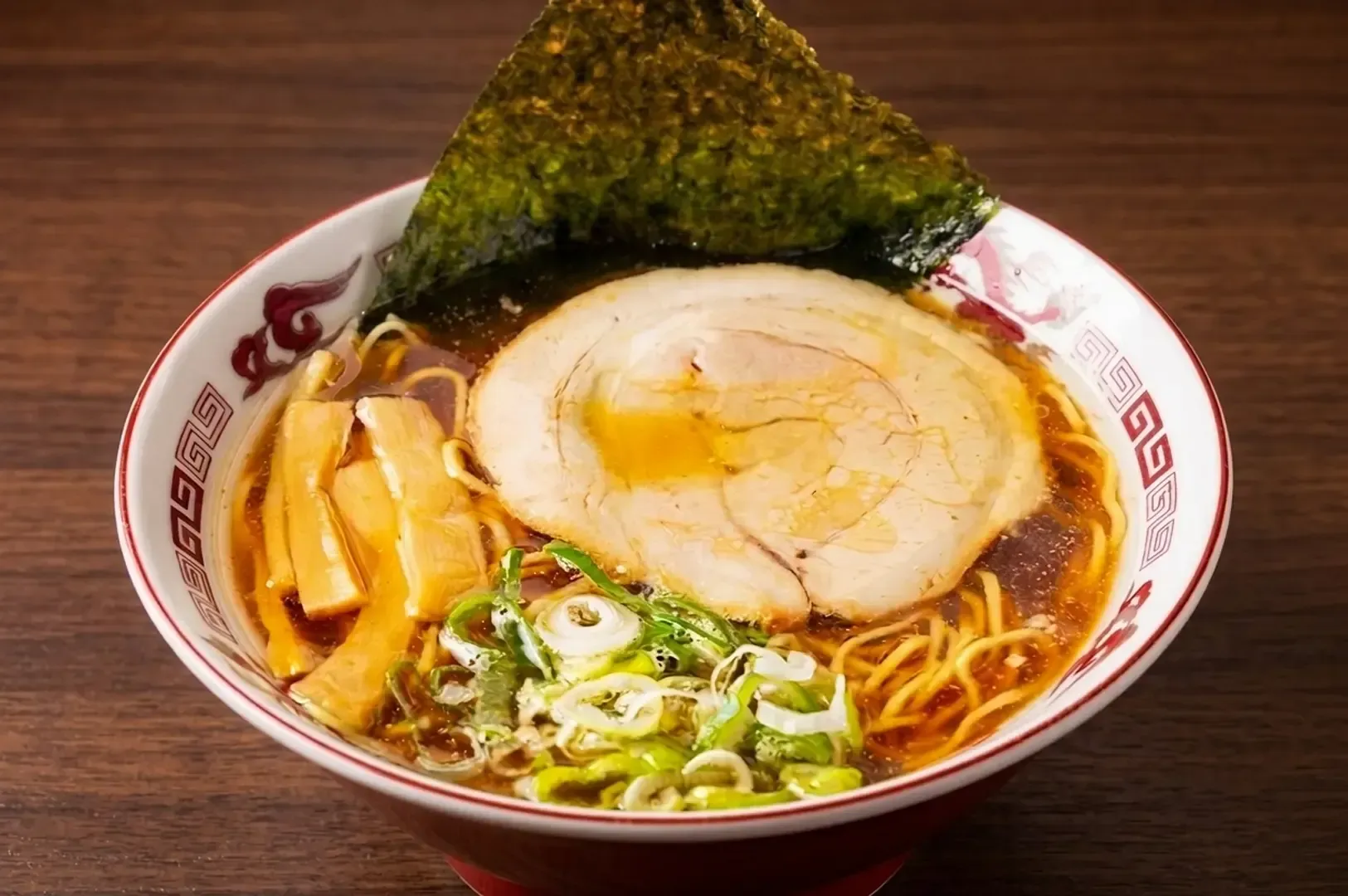 Bowl of Asahikawa shoyu ramen with thick chashu, bamboo shoots, nori, and signature lard layer on broth