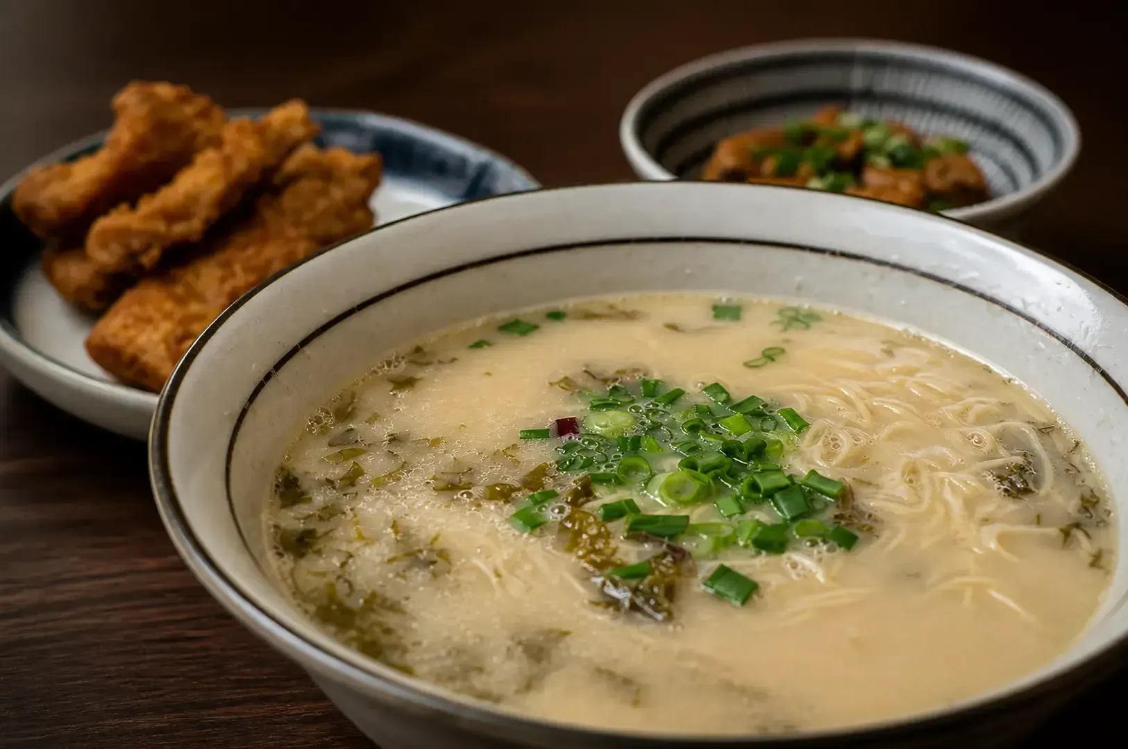 Bowl of clear broth ramen topped with chopped green onions, served with side plate of fried fish cakes