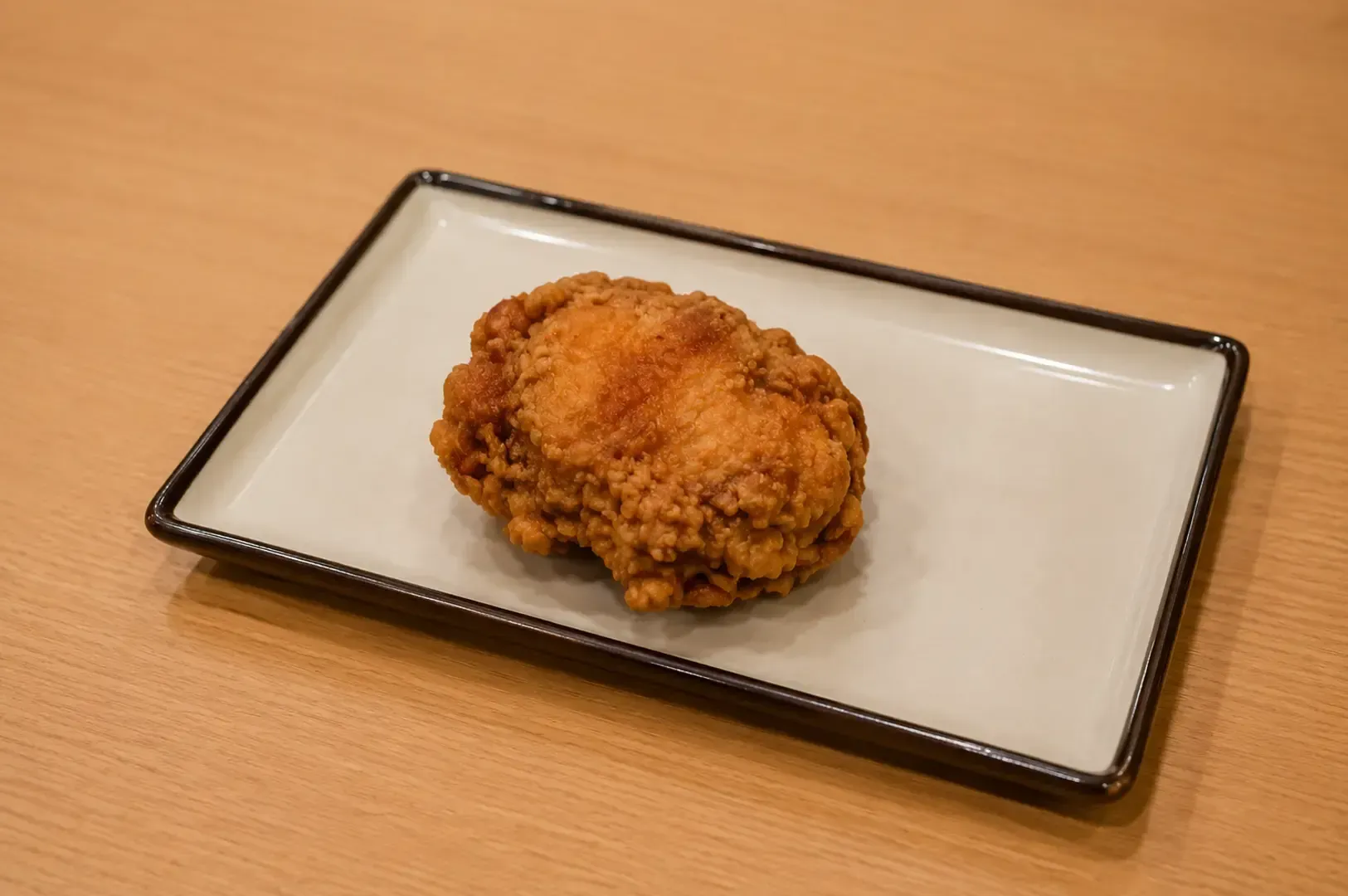 A piece of crispy Japanese fried chicken  served on a rectangular white plate with a dark rim