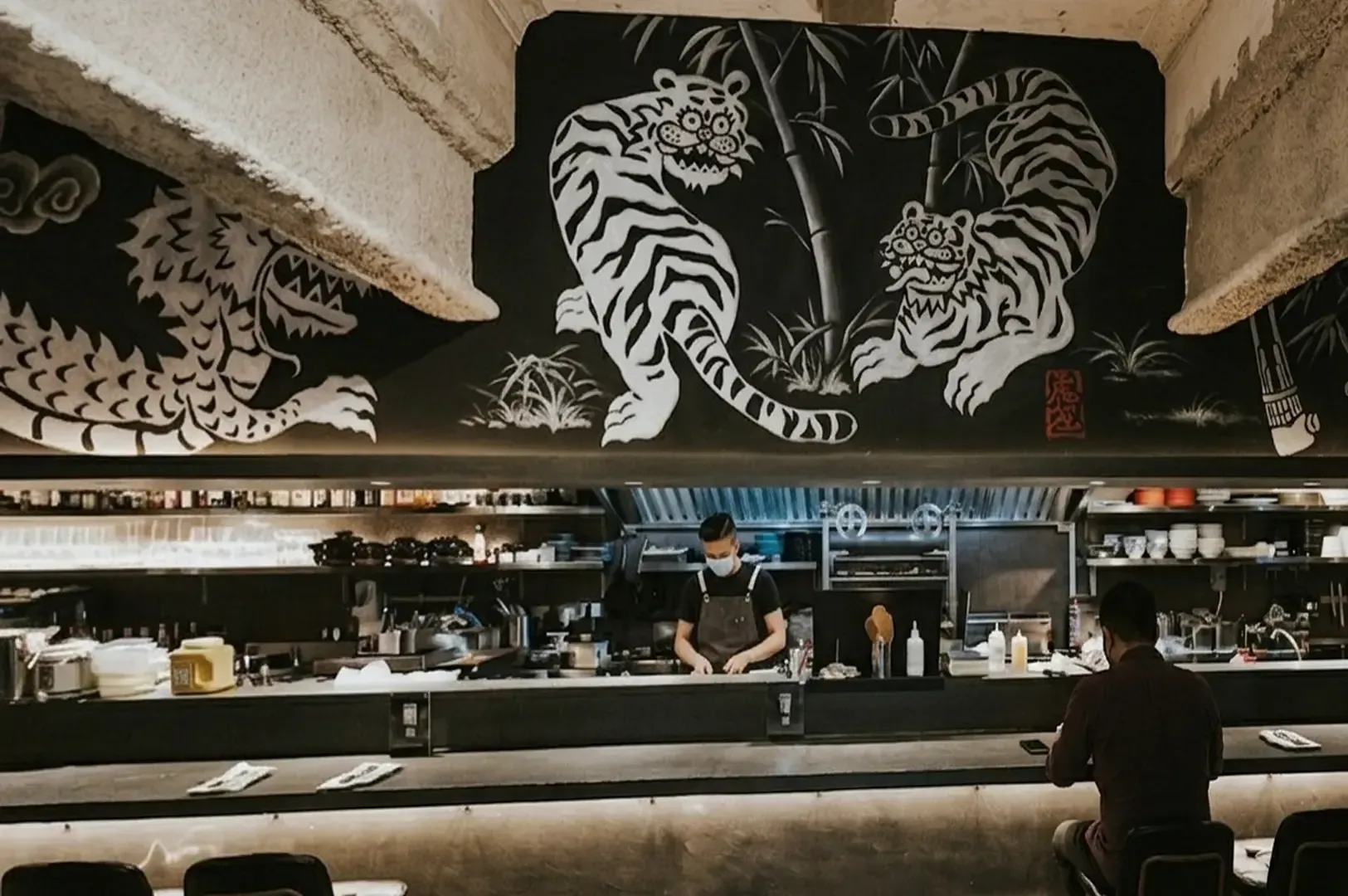 Interior view of Torasho Ramen showing the open kitchen counter with a large white tiger mural on the black wall above