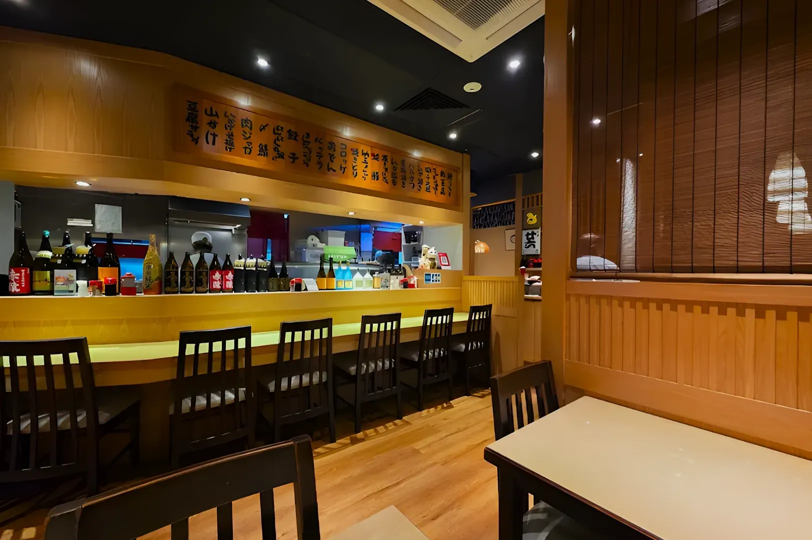 Cozy Japanese restaurant interior with a wooden counter, rows of sake bottles, and bar stools. Soft lighting and Japanese script enhance the inviting atmosphere.