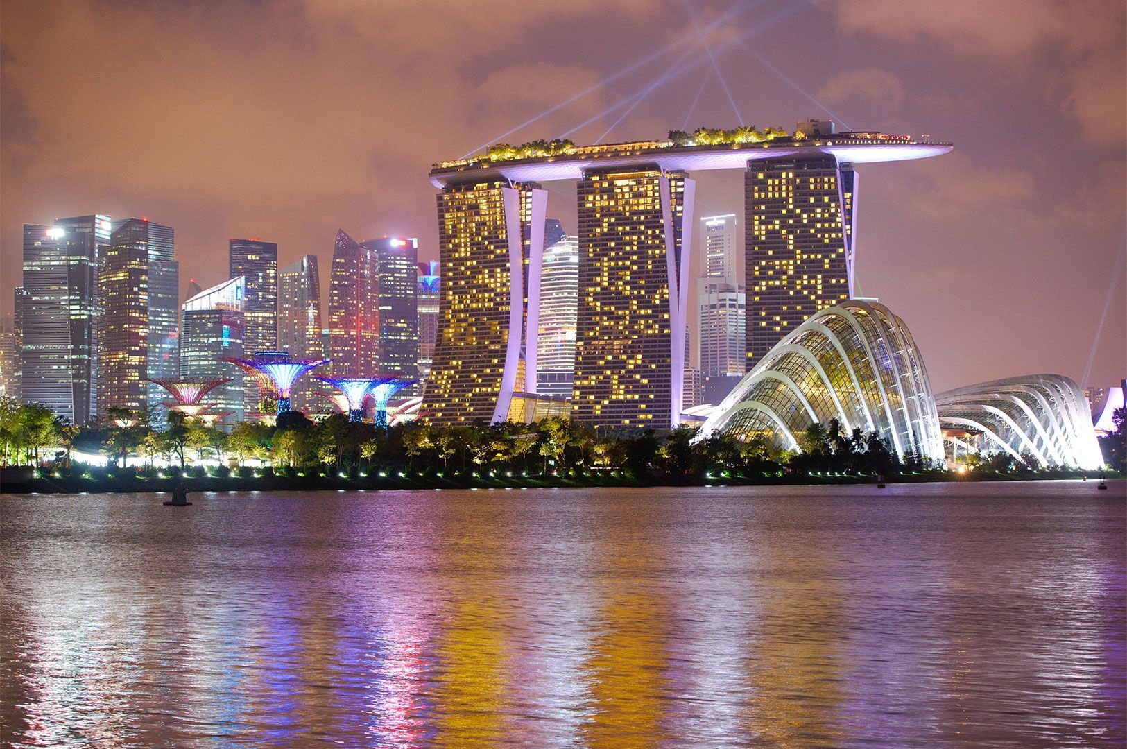 Nighttime panoramic view of the Singapore skyline, highlighting the illuminated Marina Bay Sands hotel and the white, arched domes of the Gardens by the Bay.