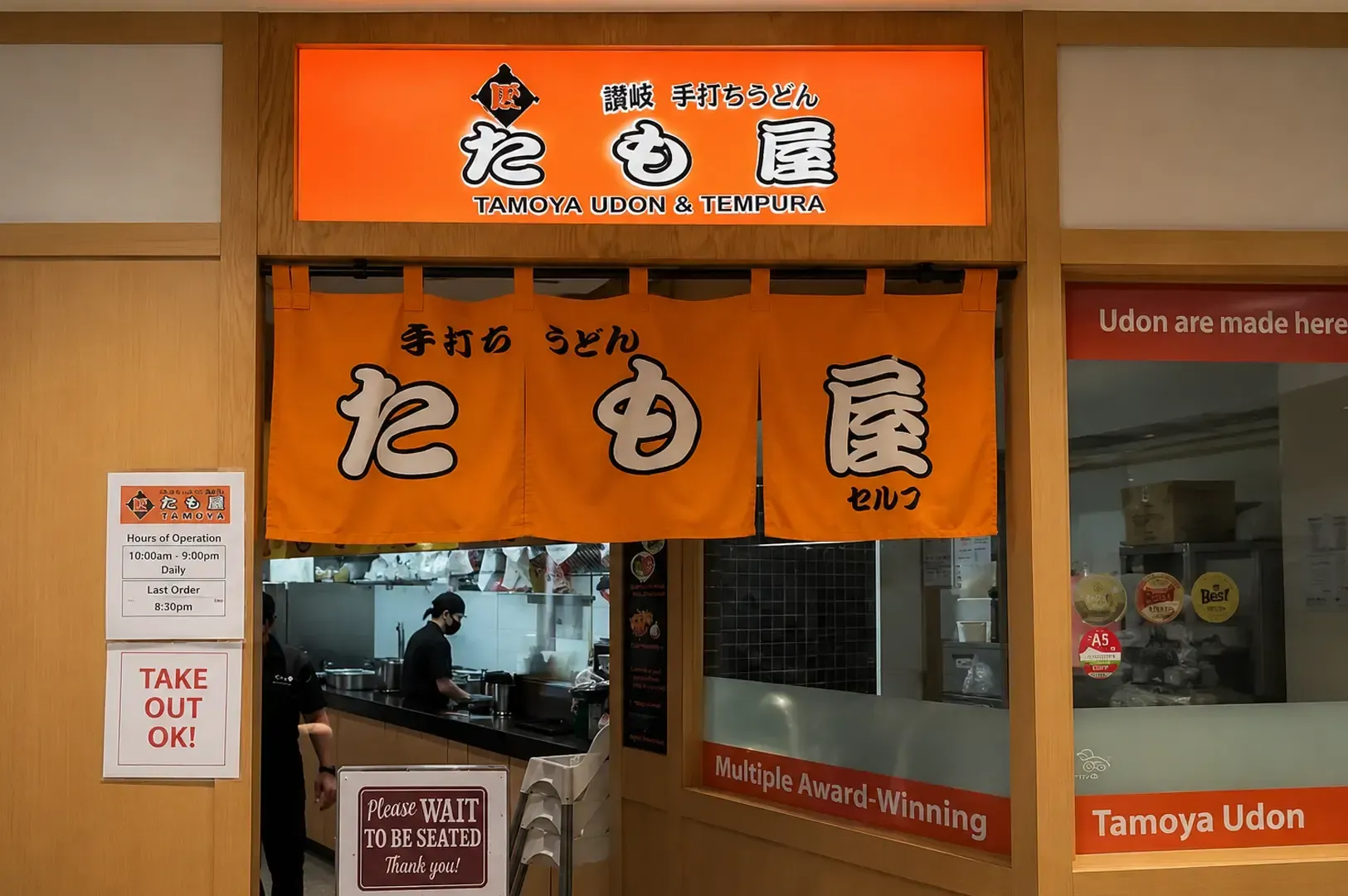 Tamoya Udon & Tempura featuring a bright orange sign, traditional noren curtains, and a view into the open kitchen