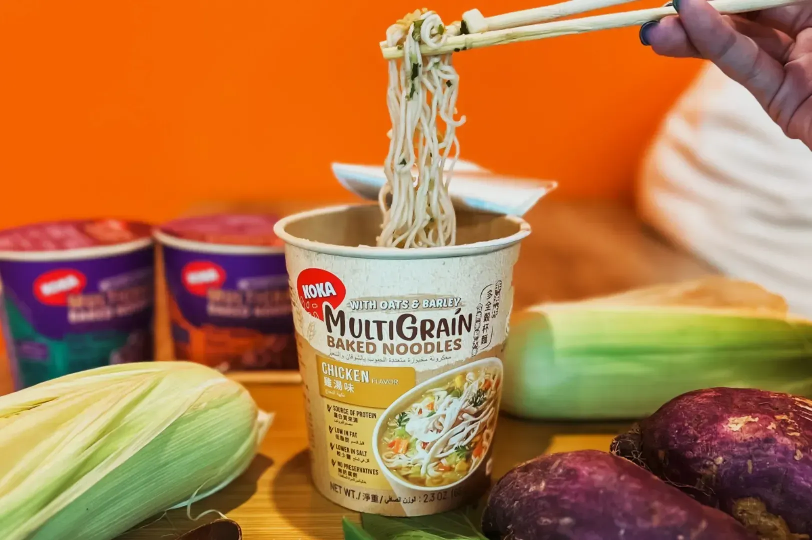 A hand uses chopsticks to lift multigrain noodles from a cup labeled 