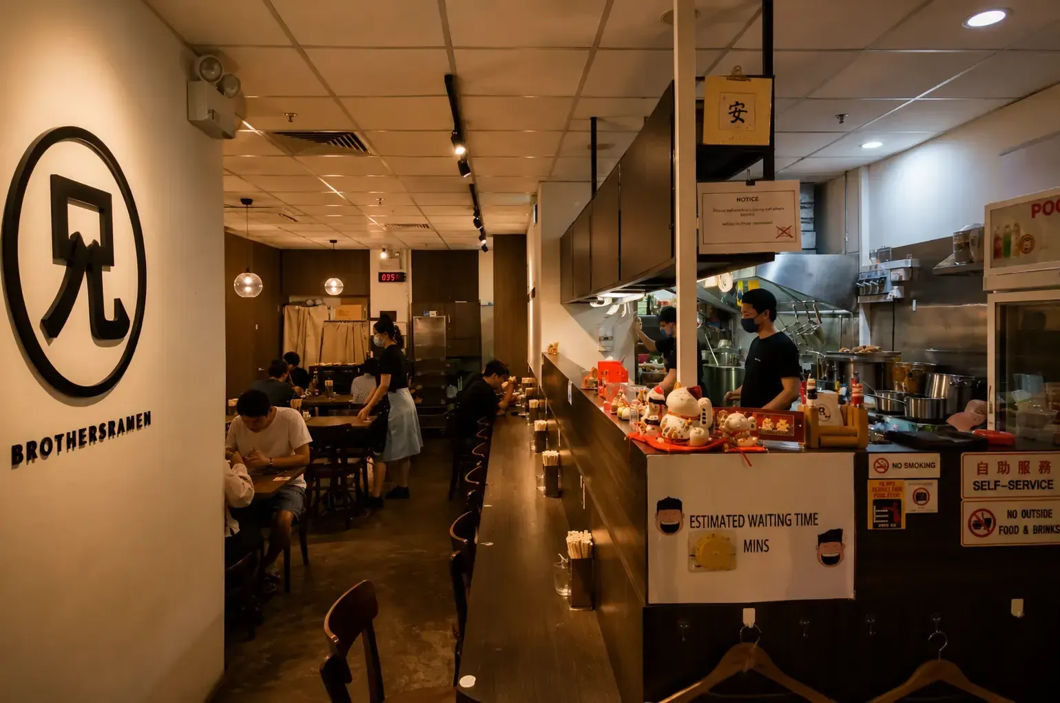 Inside a cozy ramen restaurant featuring counter seating, dining tables, and staff behind the kitchen counter.