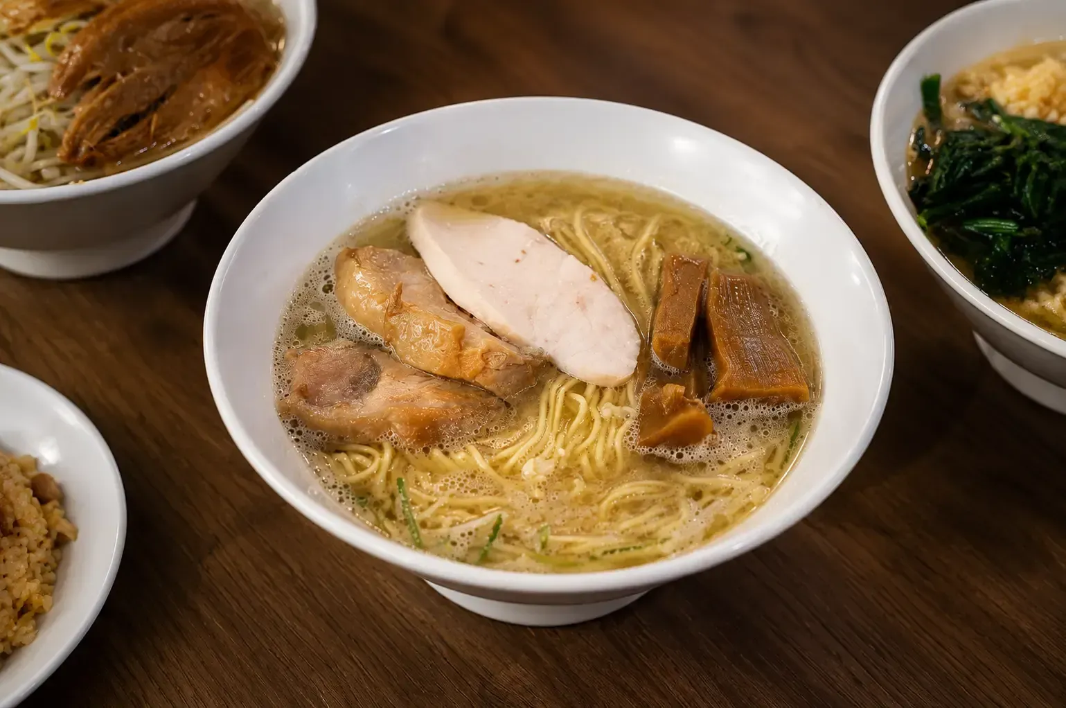 Bowl of ramen in rich broth topped with sliced chicken breast, chashu pork, and bamboo shoots.