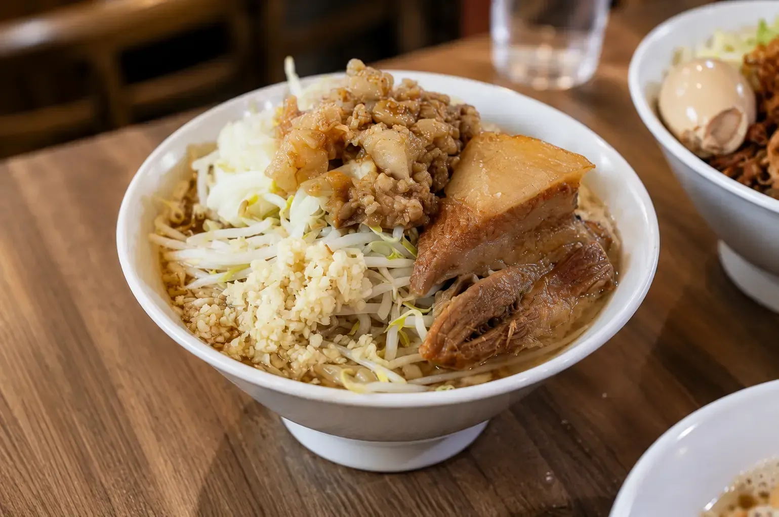 Hearty bowl of Jiro-style ramen piled high with thick pork belly, bean sprouts, and minced garlic.