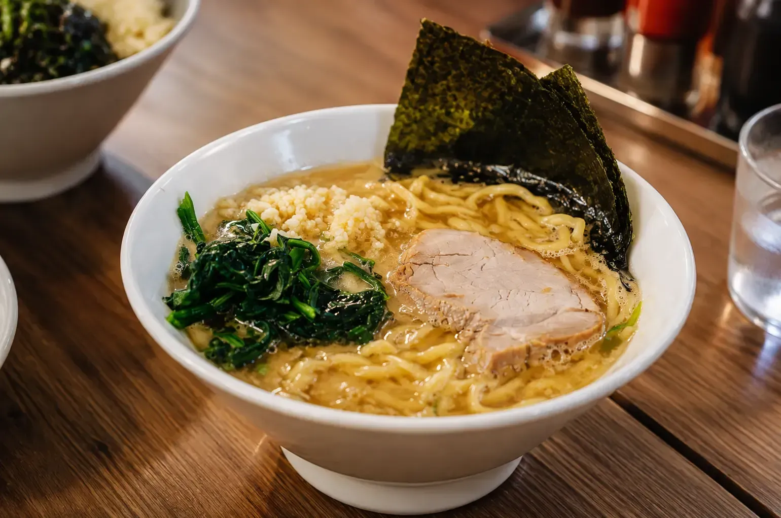 Bowl of ramen topped with a slice of chicken chashu, spinach, garlic, and nori seaweed.