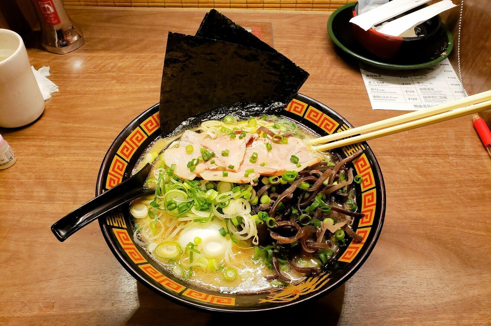 A bowl of ramen topped with chopsticks resting on the rim, showcasing the dish's rich ingredients and presentation.
