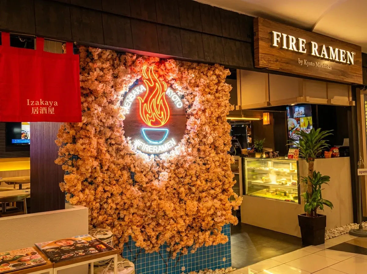 Exterior of Fire Ramen restaurant with wooden signage, a red noren banner, and a wall of pink cherry