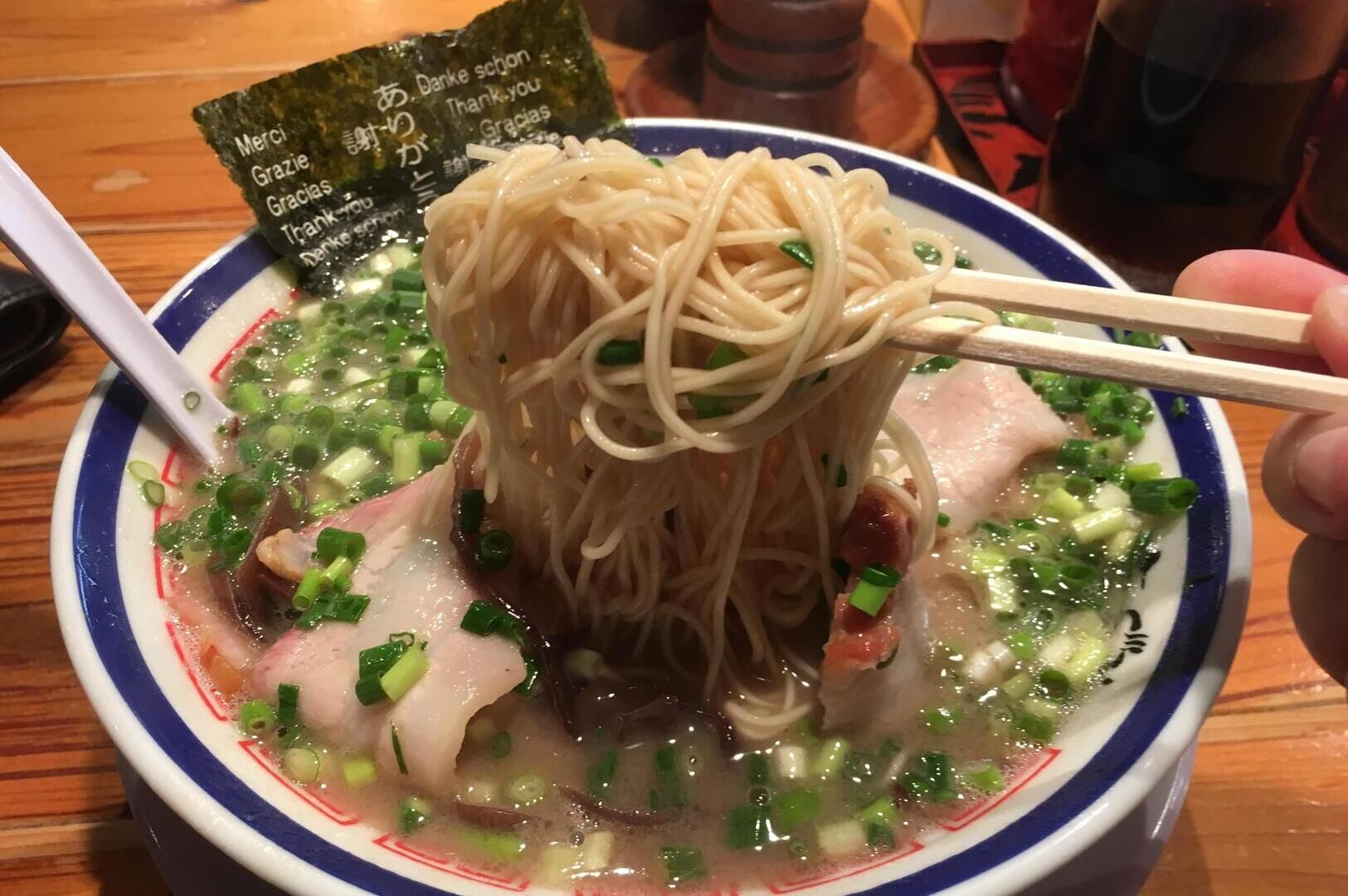 A person holding chopsticks above a bowl of Hakata ramen, showcasing the dish's rich ingredients.