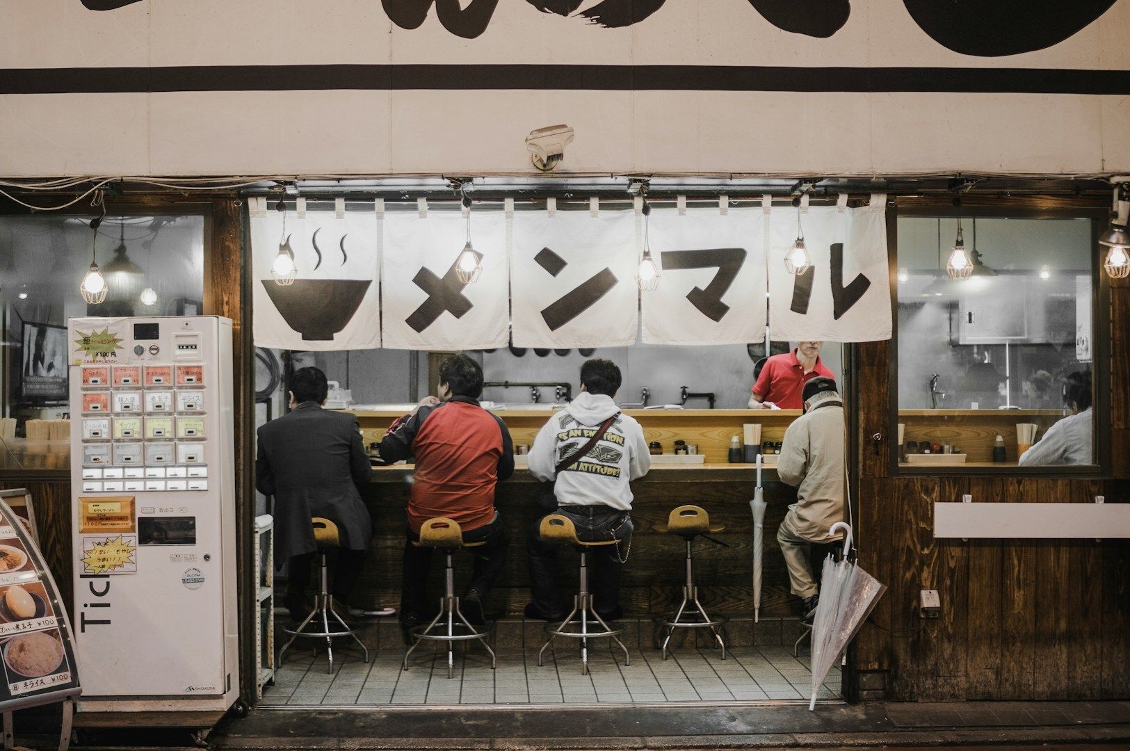 Diners gathered at a ramen shop, sitting at a table and sharing a meal in a lively restaurant atmosphere.