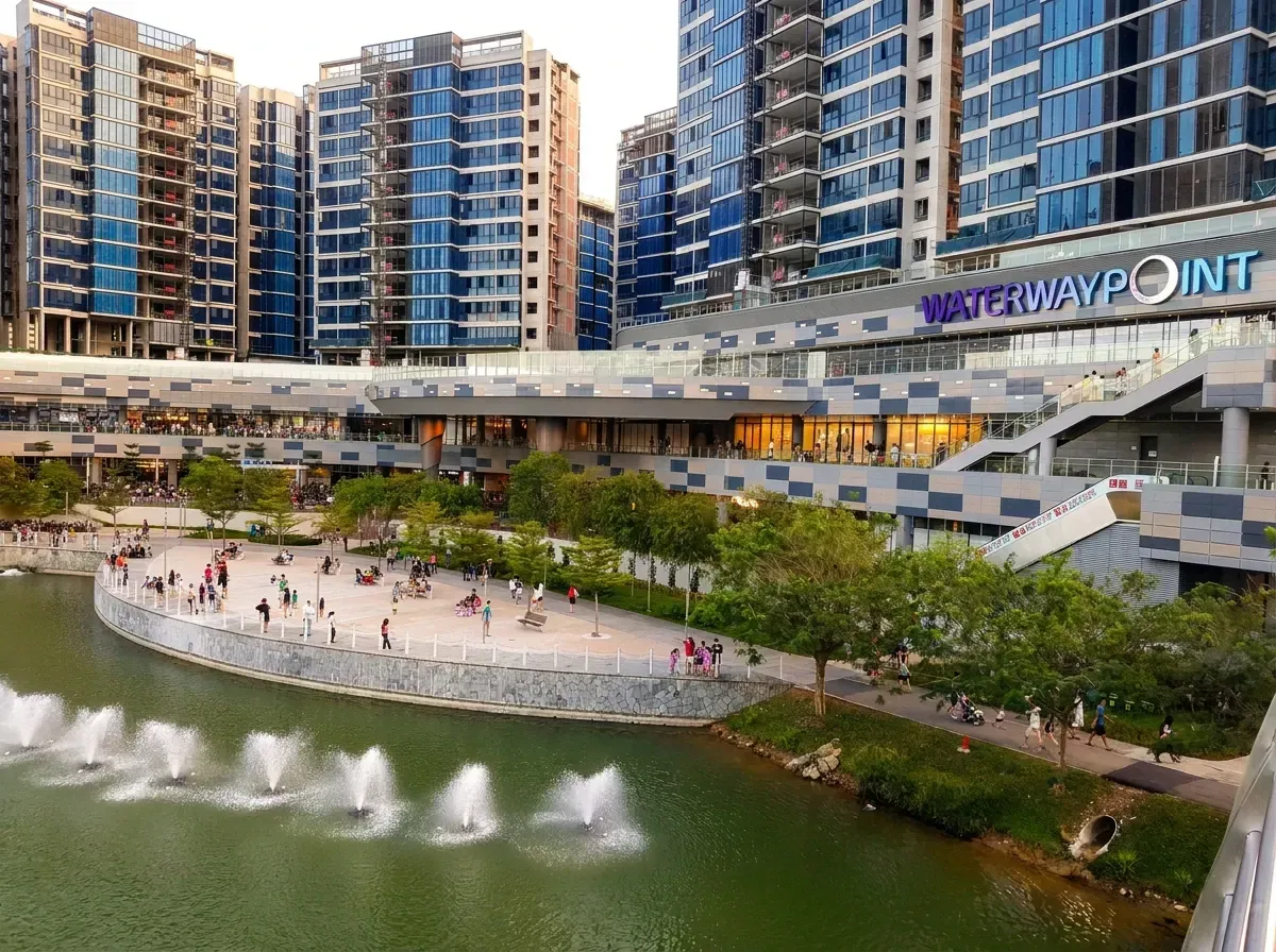 Wide view of Waterway Point shopping mall with a waterfront plaza, fountains, and high-rise apartment buildings.
