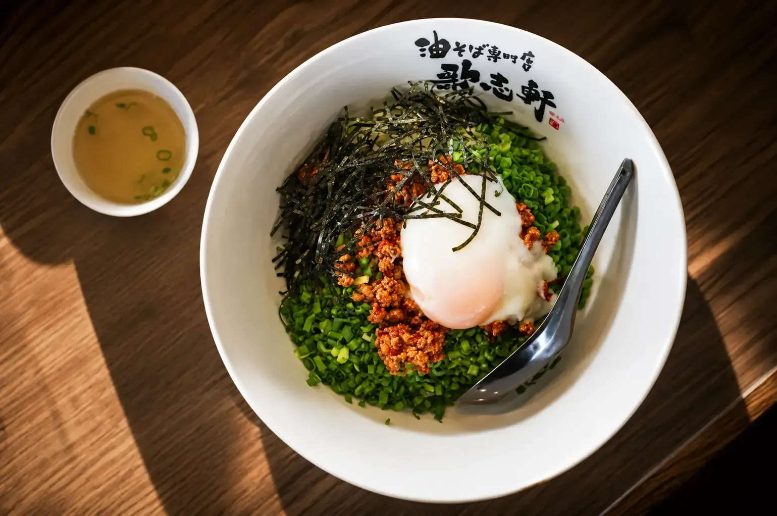Top-down view of a bowl of Kajiken mazesoba topped with minced meat, soft-boiled egg, shredded seaweed, and green onions.