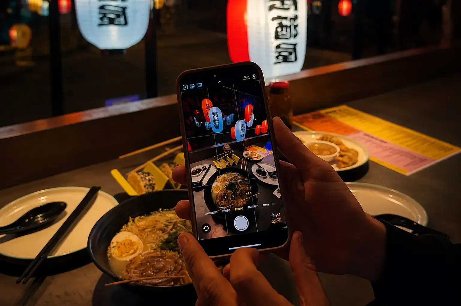 A customer taking a smartphone photo of a steaming bowl of ramen at a cozy.