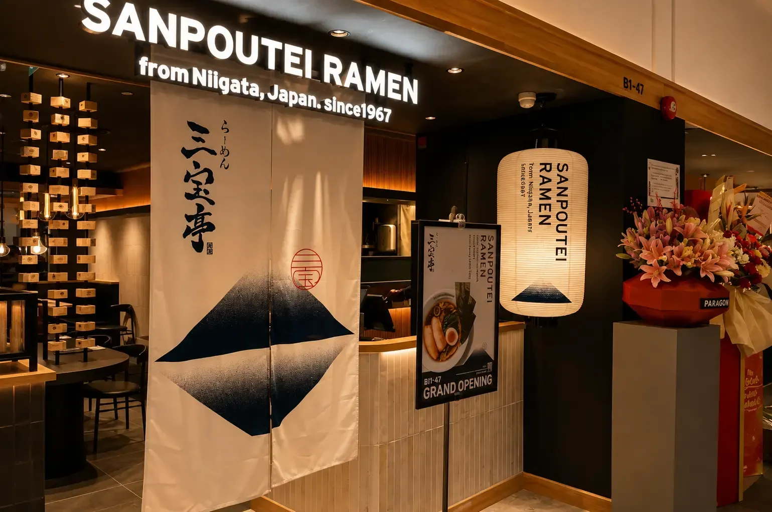 Entrance to Sanpoutei Ramen featuring a white noren curtain, a large paper lantern, and a grand opening sign stand.