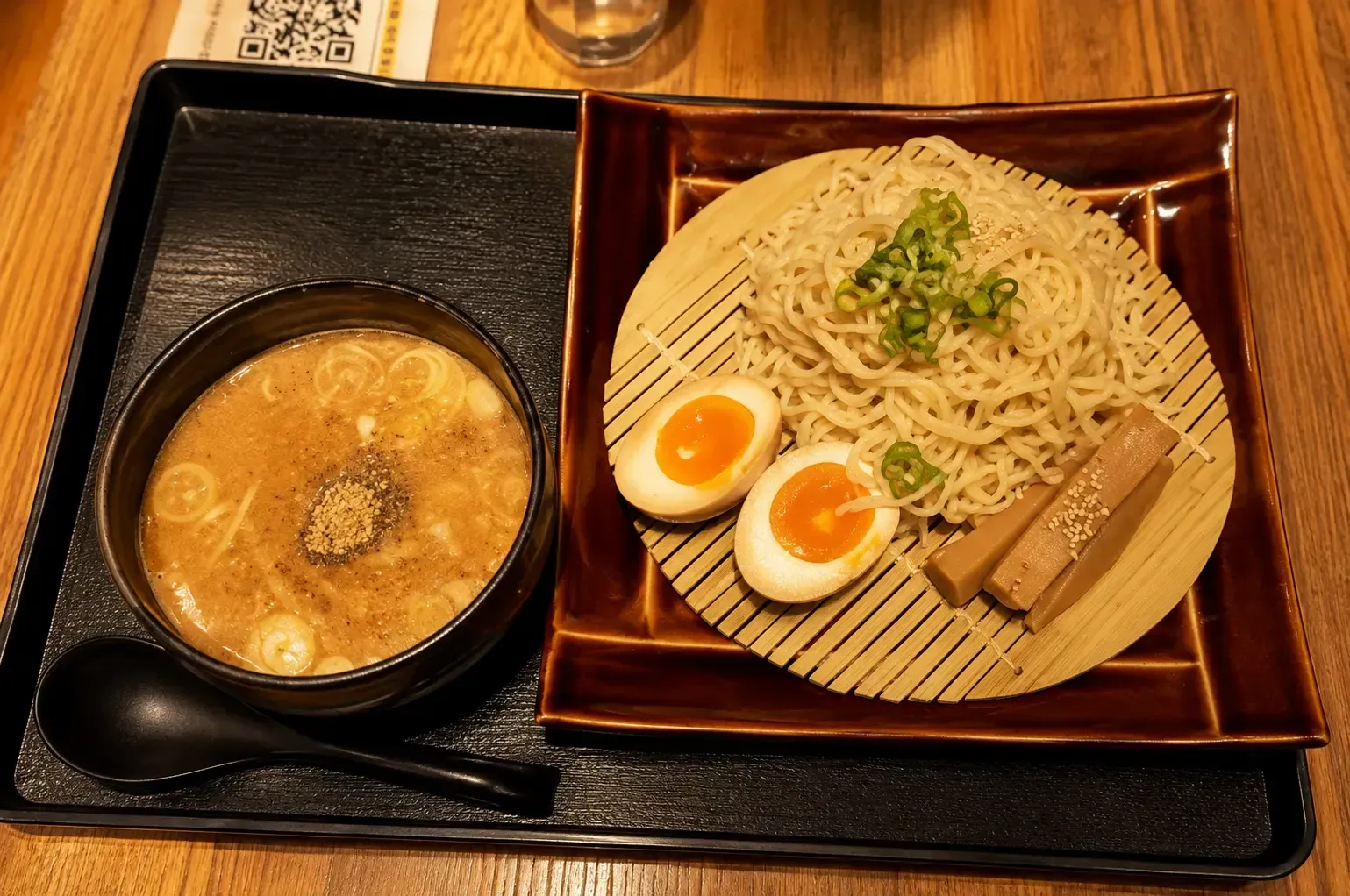 Dipping ramen set featuring a plate of cold noodles, soft-boiled eggs, and bamboo shoots alongside a bowl of hot dipping broth.