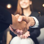 A man and a woman are shaking hands in front of a woman.