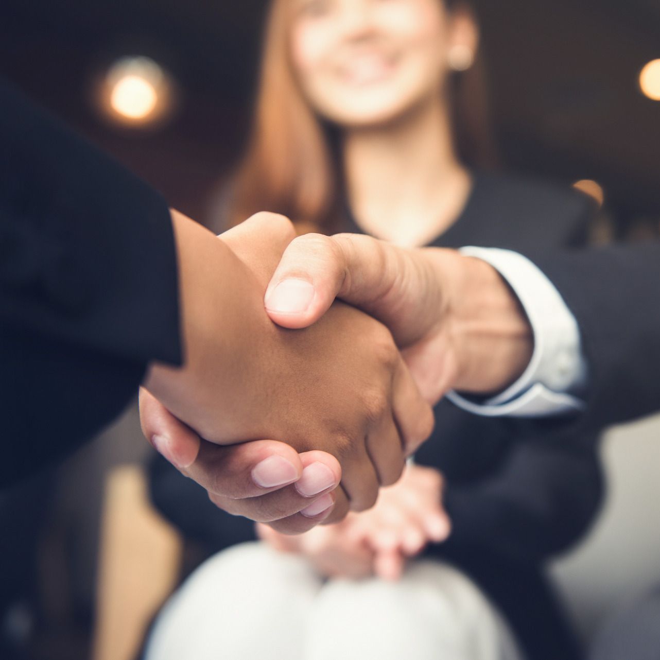 A man and a woman are shaking hands in front of a woman.