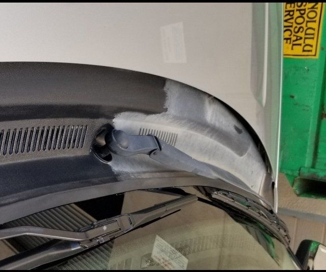 Black car windshield base with wiper blades, partially painted white. Yellow recycling bin in background.