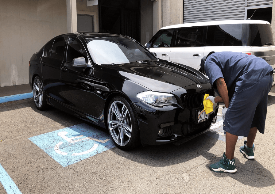 Person cleaning a shiny black BMW sedan parked in a handicapped spot.