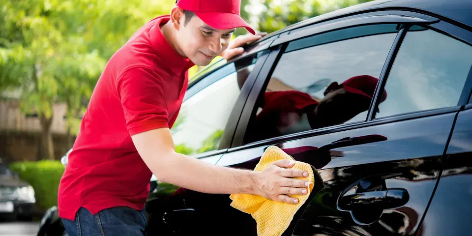 Man in red cap and shirt cleaning a black car with a yellow cloth.