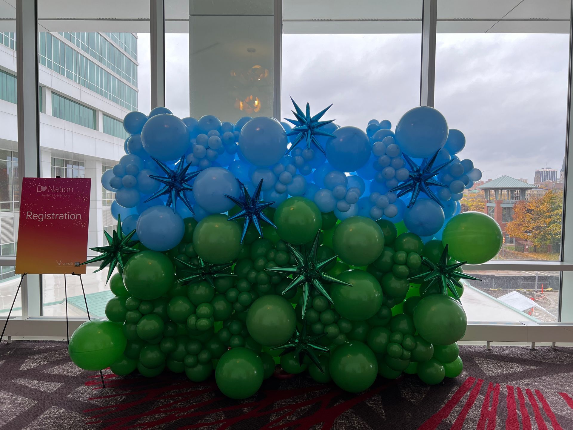 A wall of blue and green balloons in front of a window.