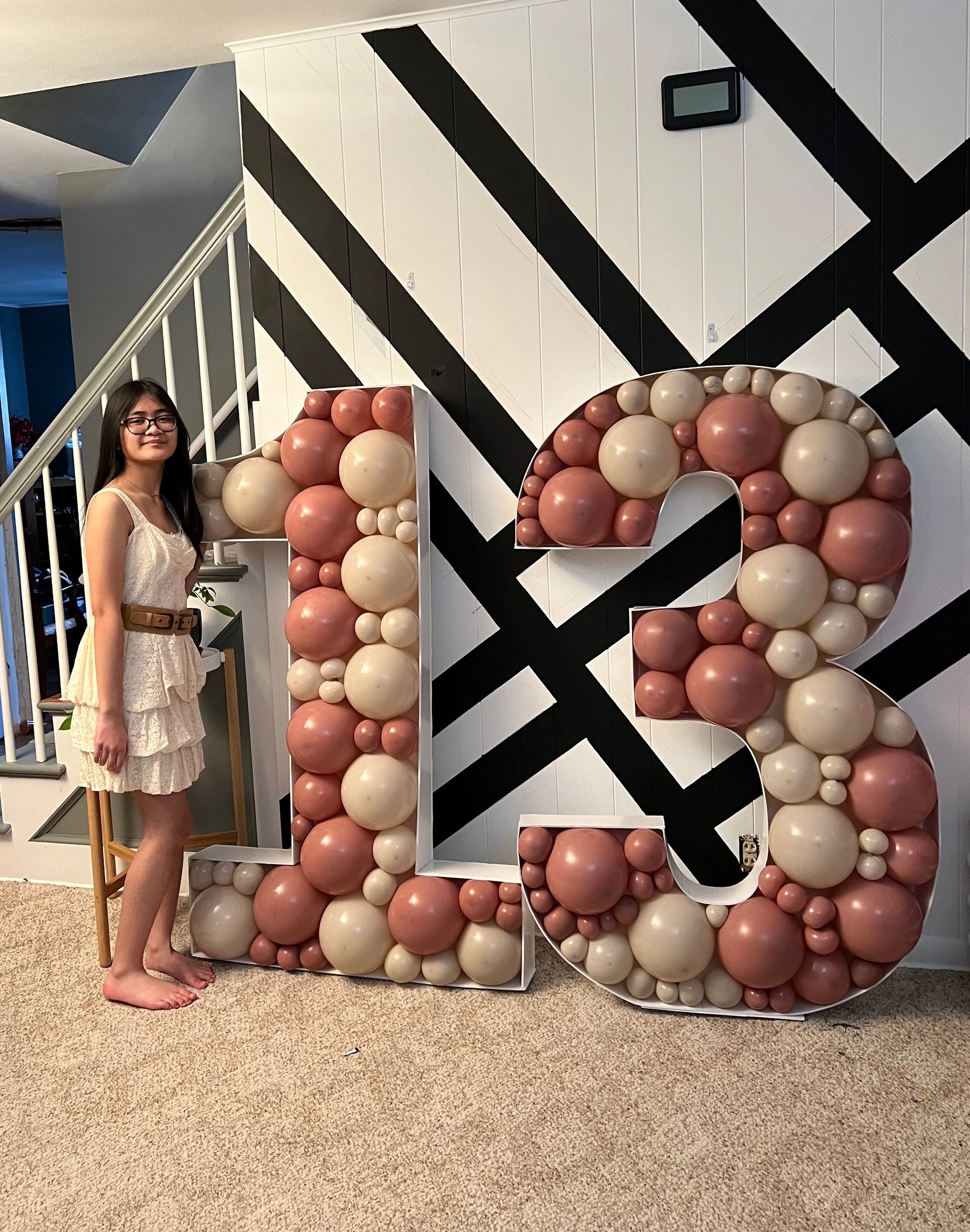 A woman is standing next to a large number made of balloons.