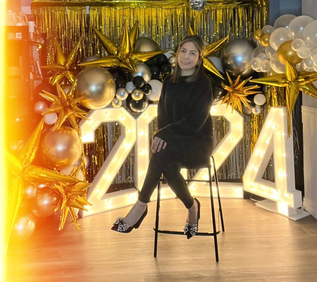 A woman is sitting on a stool in front of a sign that says 2024.