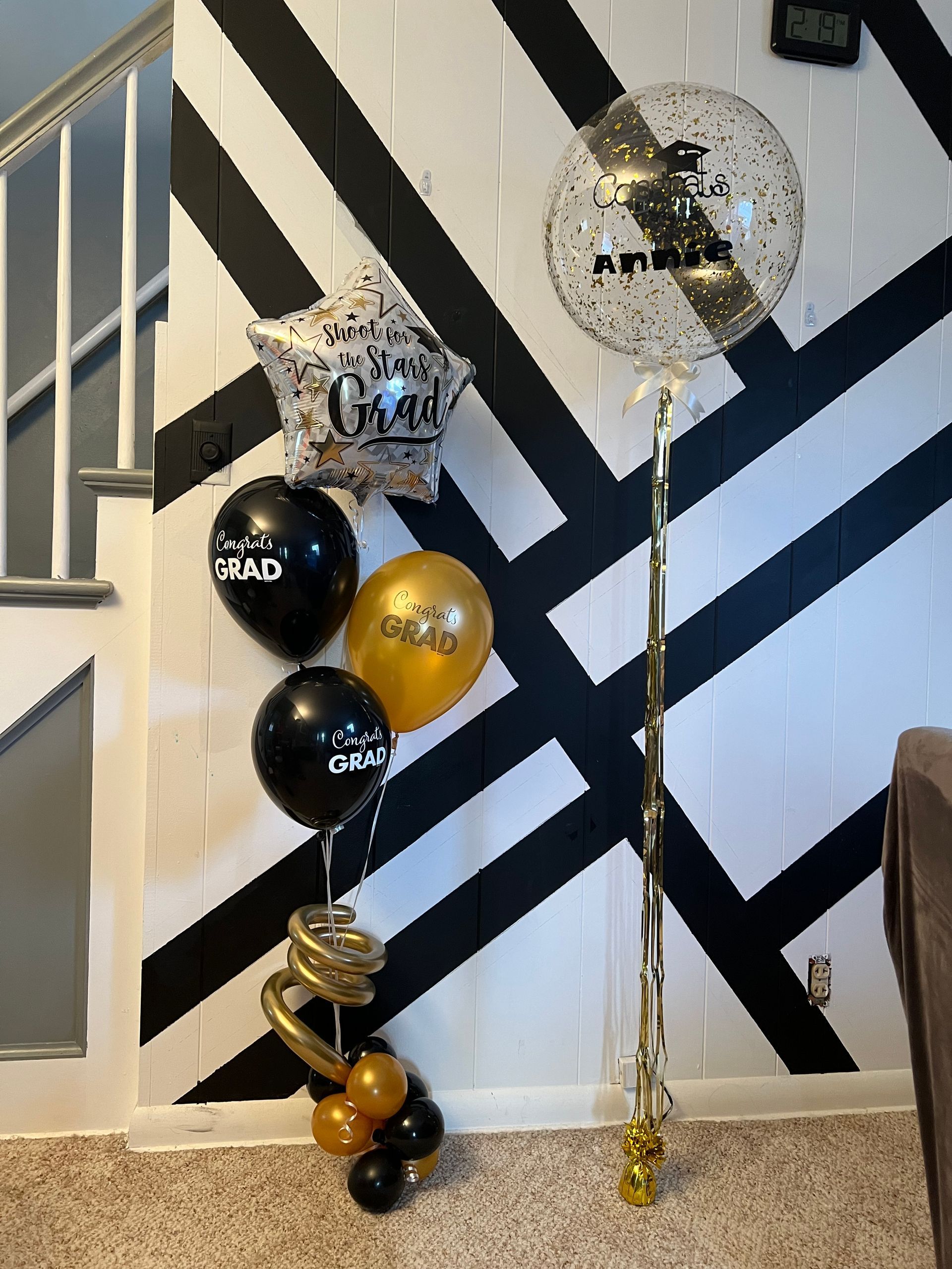 Black, gold, and silver balloon arrangement by a staircase with bold black-and-white wall stripes