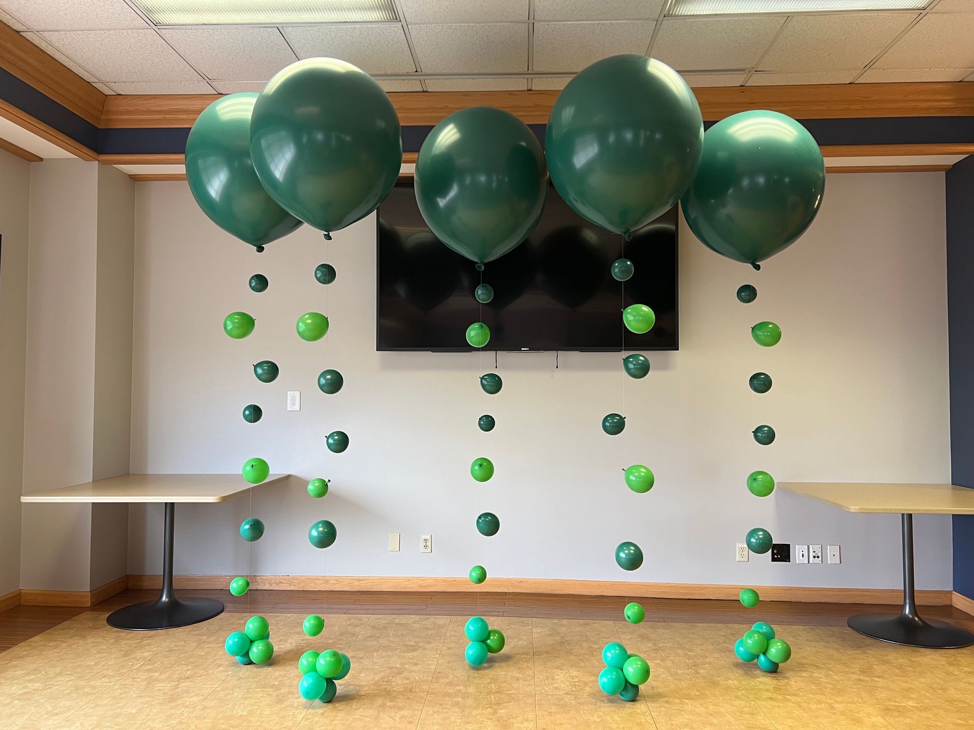 A bunch of green balloons are hanging from the ceiling in a room.
